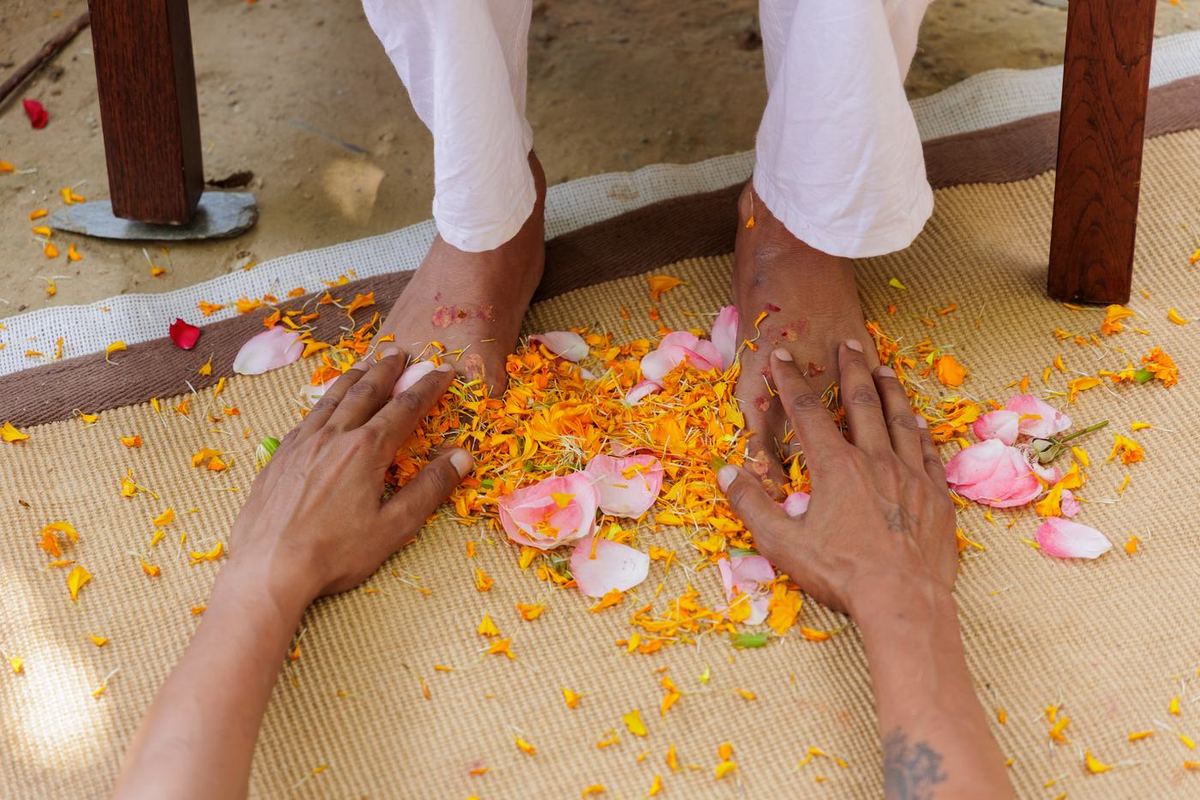 A disciple's hands resting at the Guru's feet among marigold and rose petals